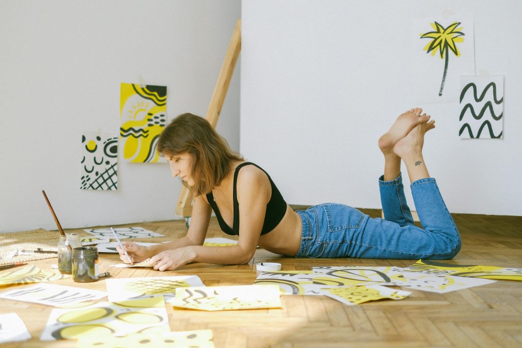 A focused woman lying on the floor creating artistic illustrations indoors.