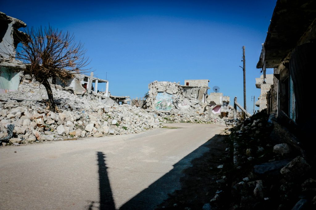 Destroyed buildings and rubble in a deserted street of Idlib, Syria, under clear blue sky.
